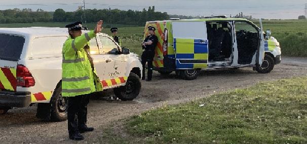 GBC and Kent Police Vehicle parked by side of road with field behind. Police officers signalling right arm to stop.