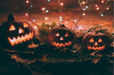 3 carved out pumpkins lit up with candles inside, in front of a backdrop of orange lights.