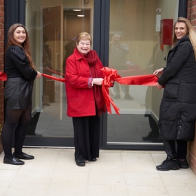 Cllr Jenny Wallace cutting a red ribbon outside new council homes.