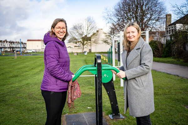 2 ladies standing on outdoor park equipment in a park