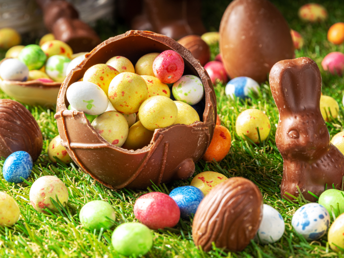 Bright easter scene of a basket with eggs, sitting on green grass with brown chocolate easter bunnies.
