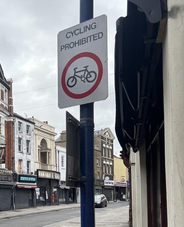 Street sign on lamp post showing cycling prohibited on a street with a car in the background