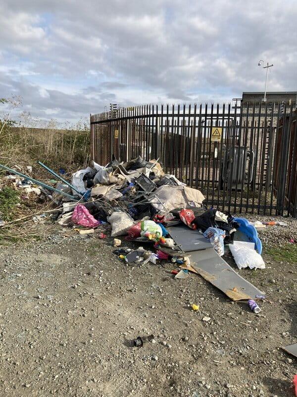 A site where waste has been fly-tipped against black railings near a power station.
