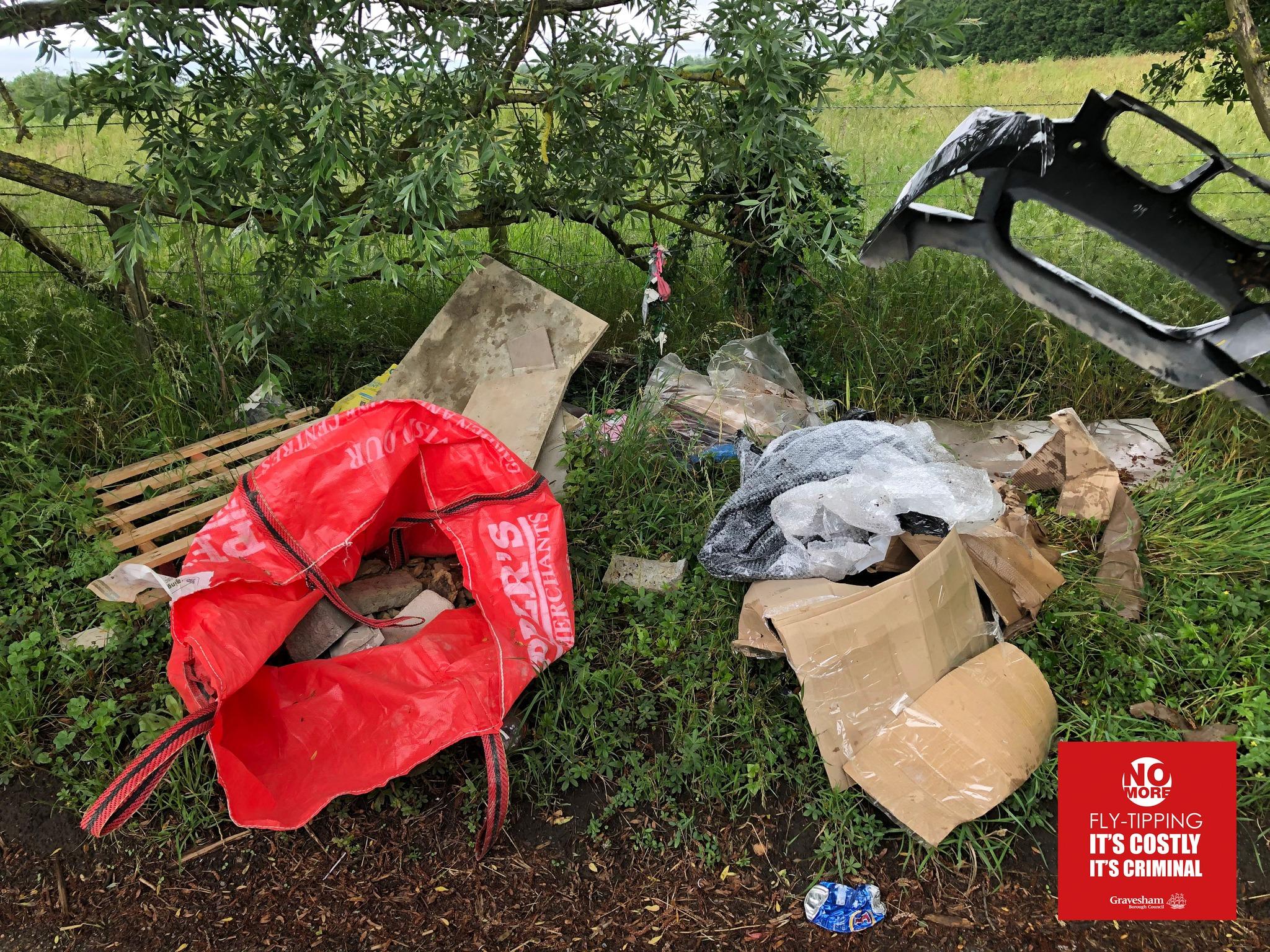 Countryside showing flytipping of waste, cardboard and rubble alongside a red waste bag.