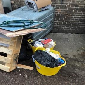 photo of rubbish fly-tipped on the side of the road in a yellow bucket and back bags