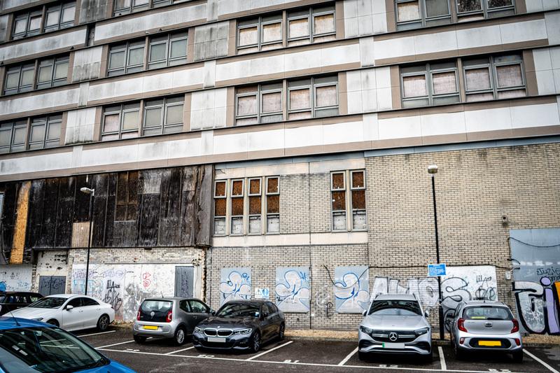 view from a car park looking at unwanted building which is in a state of disrepair with boarded windows