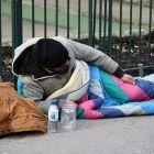 Homeless man sitting on the street in a sleeping bag.