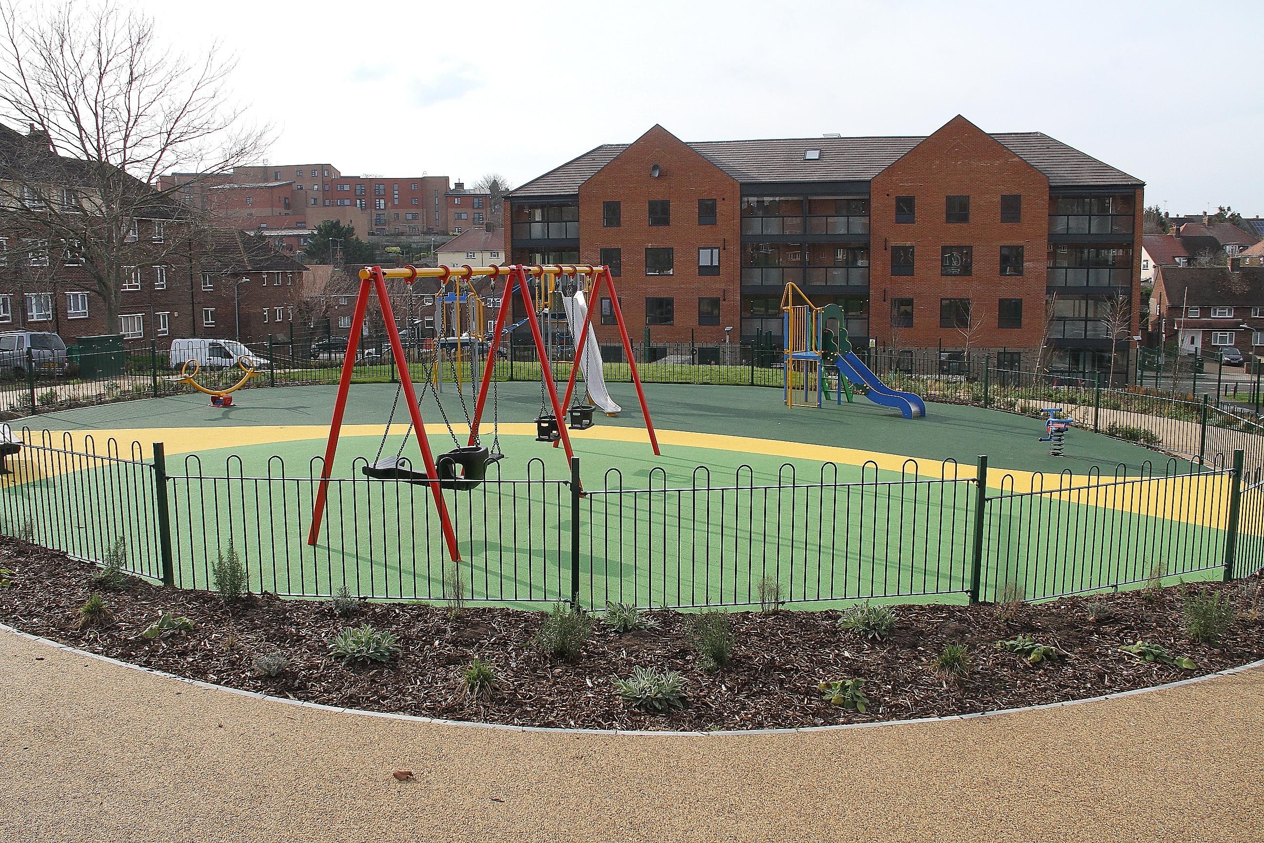 Children's swings and slide within a fenced off play area in front of a council housing block.