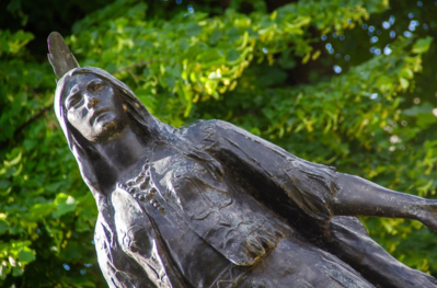 Bronze statue of Pocahontas against a green tree