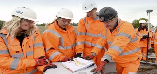 Group of construction officers standing around a project plan. Wearing orange protective clothing and hard hats.