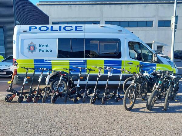 12 e scooters and 4 ebikes lined up in front of a police van which were seized.