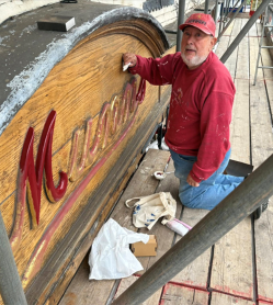 A person refurbishing the sign for a local craft shop Munns