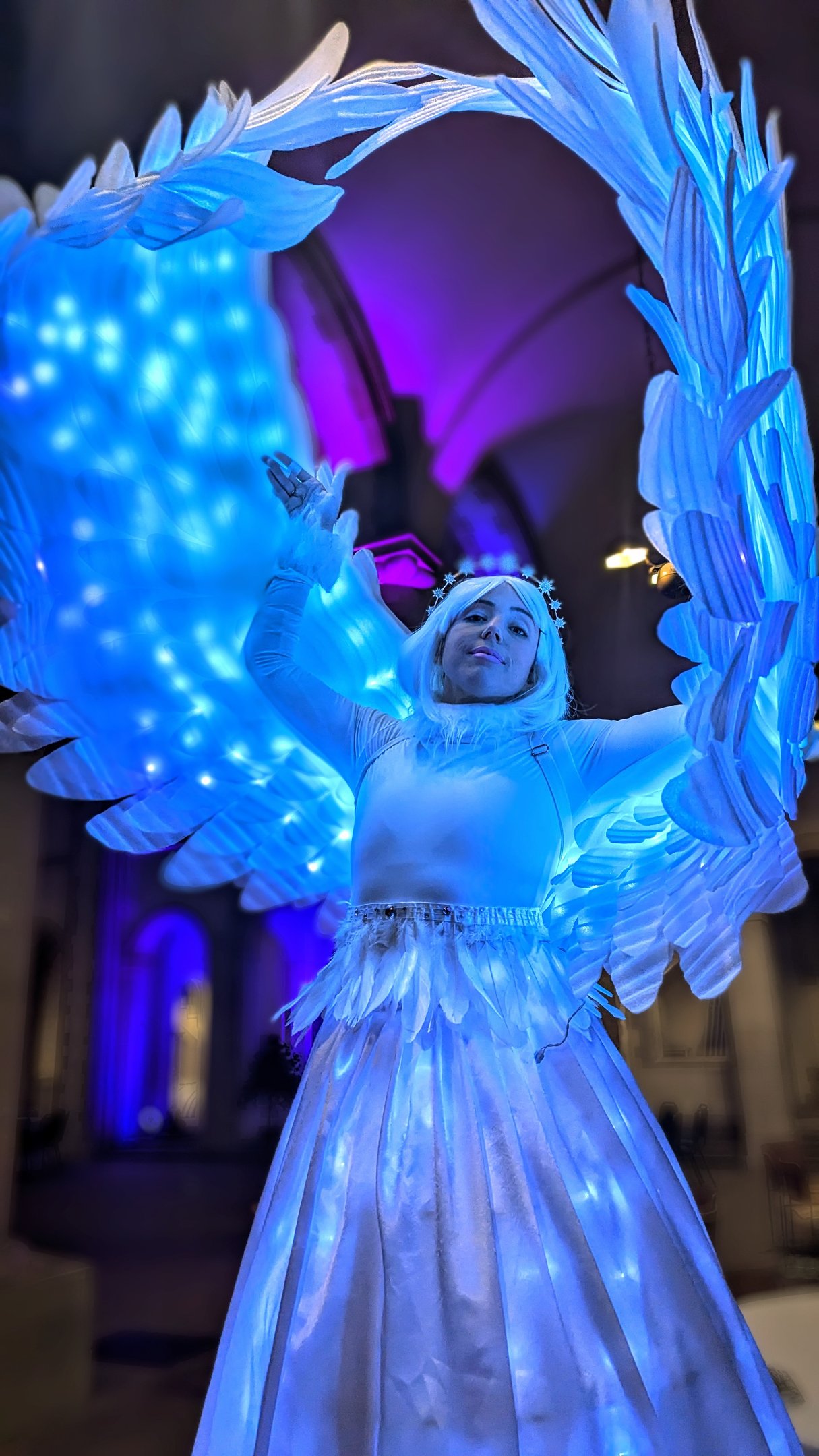 A woman in a blue and white light up snow angel costume on stilts
