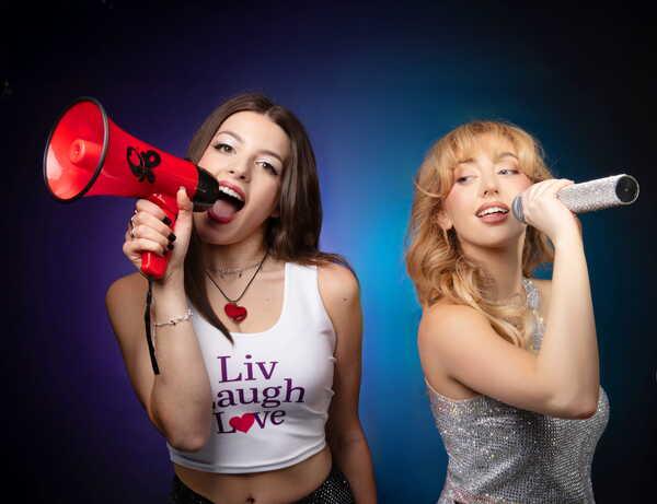 Two women next to eachother, one on the left holding a red megaphone to her open, mouth, the other holding a silver microphone.