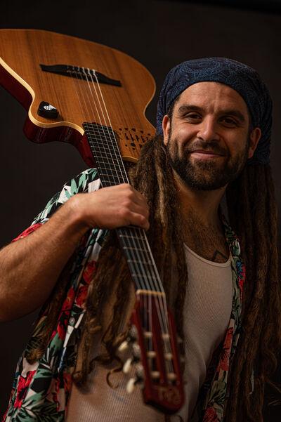 Male musician Thomas Abrahams holding guitar over his shoulder and facing the camera.