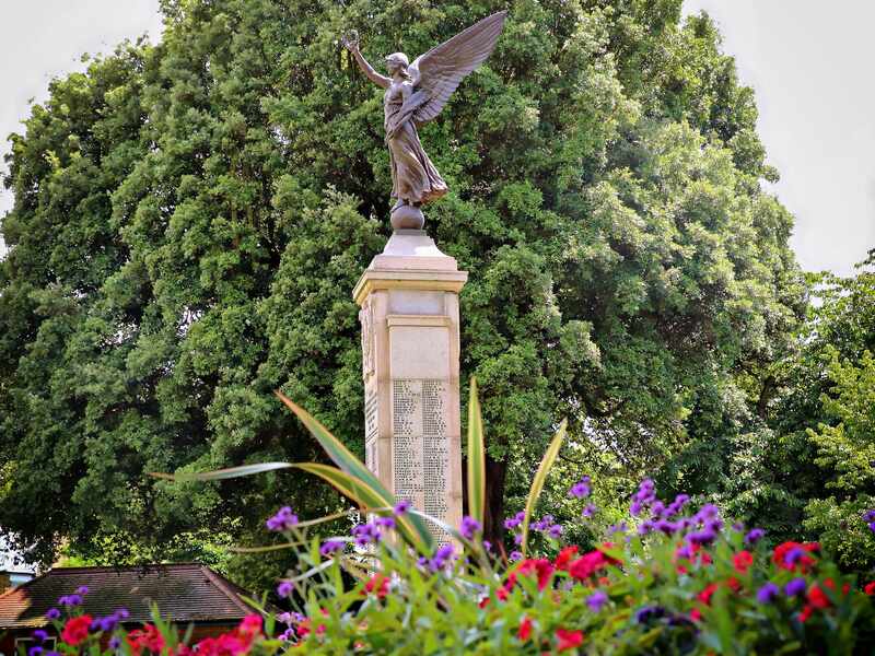 A statue for remembrance with trees in the background and flowers in the front.