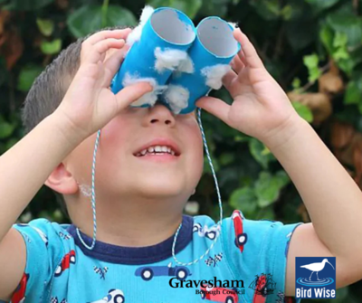 Young child holding up hand made binoculars to look up at the sky, wearing a blue tshirt.
