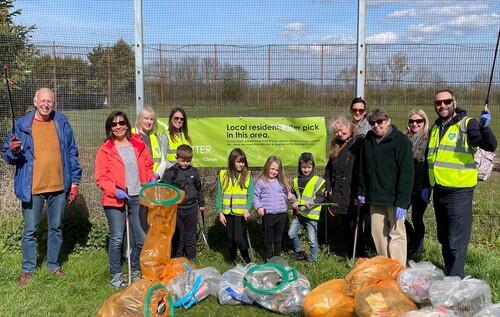 Group of 13 people, 9 adults and 4 children standing in a row with clear and orange bags of waste they have collected