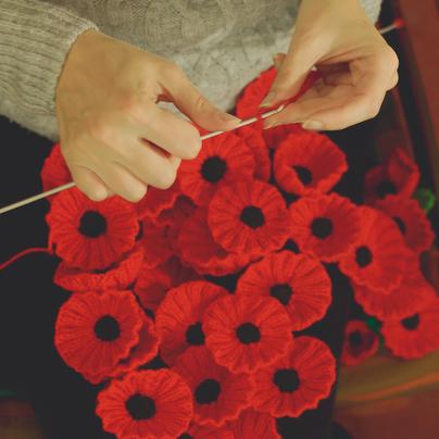 Pair of hands holding knitting needles and red thread, crocheting poppies.