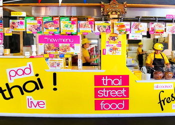 Pad Thai stall at Gravesend market. Yellow stall with menus and people standing behind working.