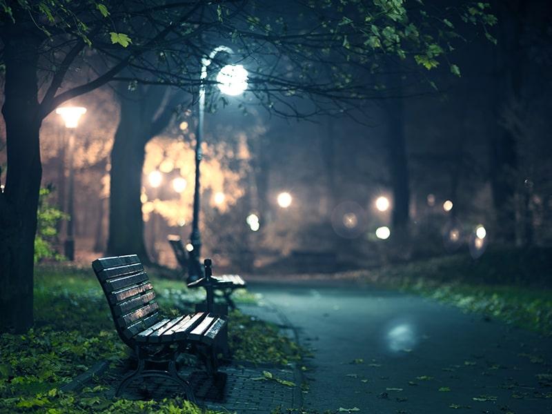 Park bench under a street lamp along a dark path at night-time.