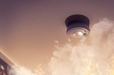 Looking up at a smoke alarm on the ceiling with smoke and flames rising