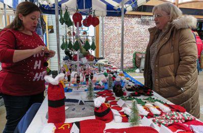 Market stall with two people standing, selling a selection of knitted goods.