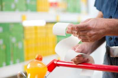 Hand holding a receipt whilst pushing a shopping cart in a drinks aisle.